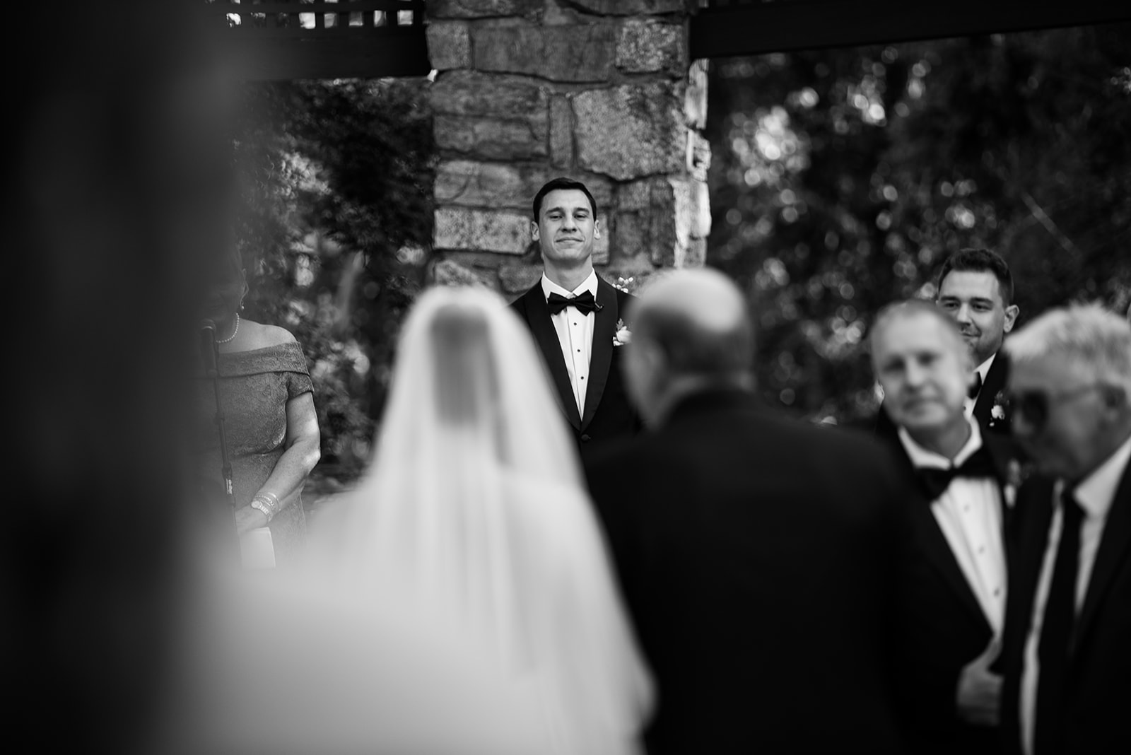 Black and white photo of an emotional groom watching his bride walk down the aisle during the ceremony.